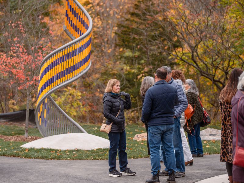People talking and standing near a piece of coloured metal artwork in a park.